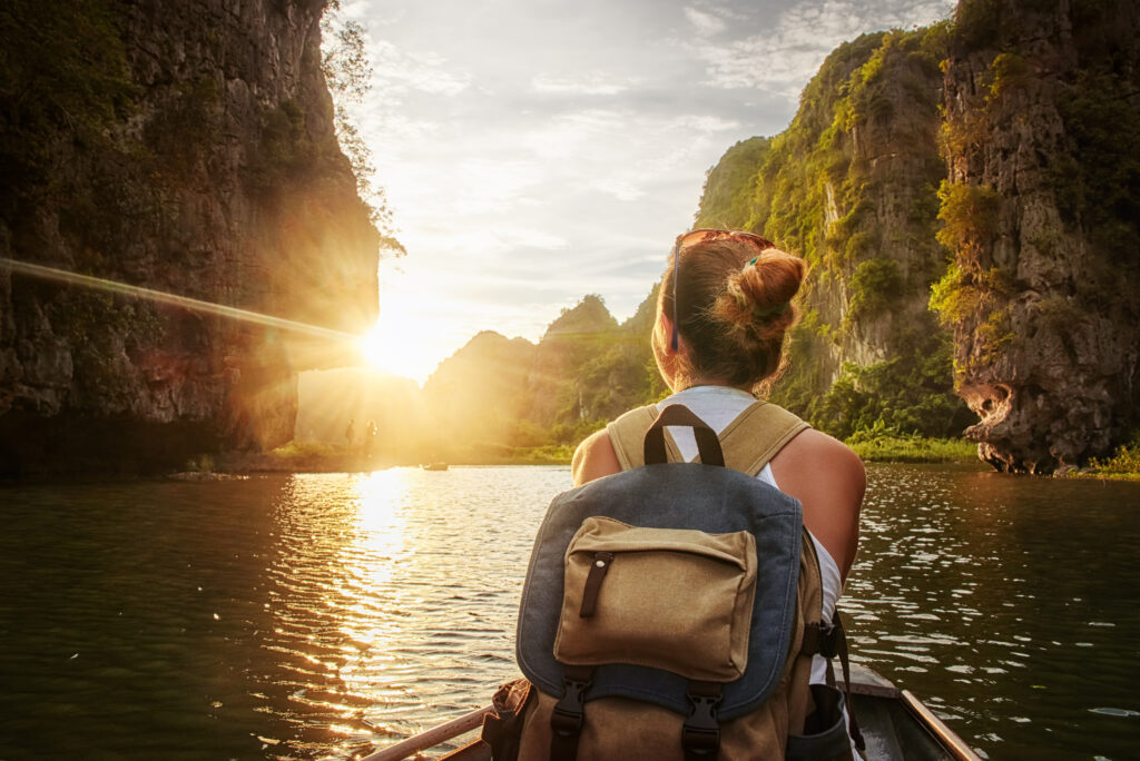Woman traveling by boat enjoying sunset among of karst mountains